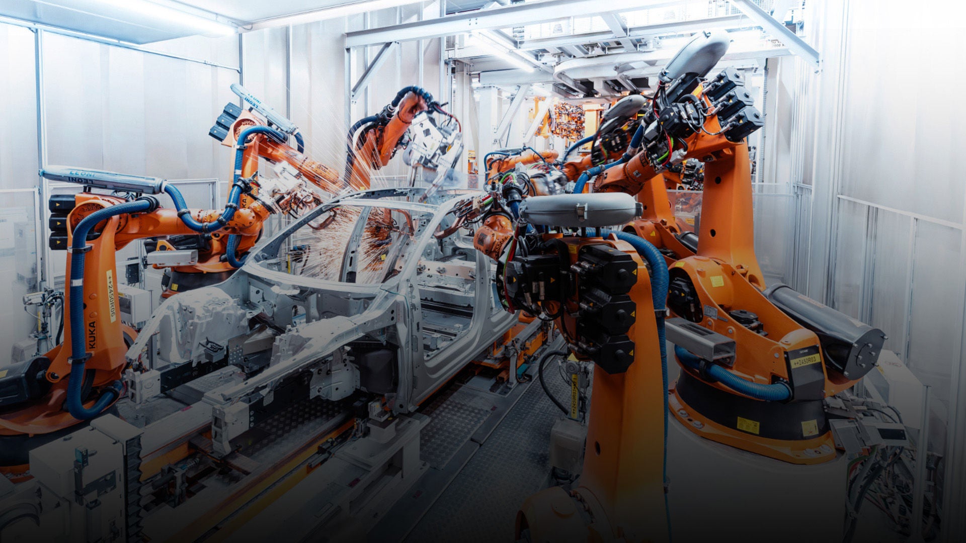 Robotic arms weld a car body in a brightly lit, automated production line.