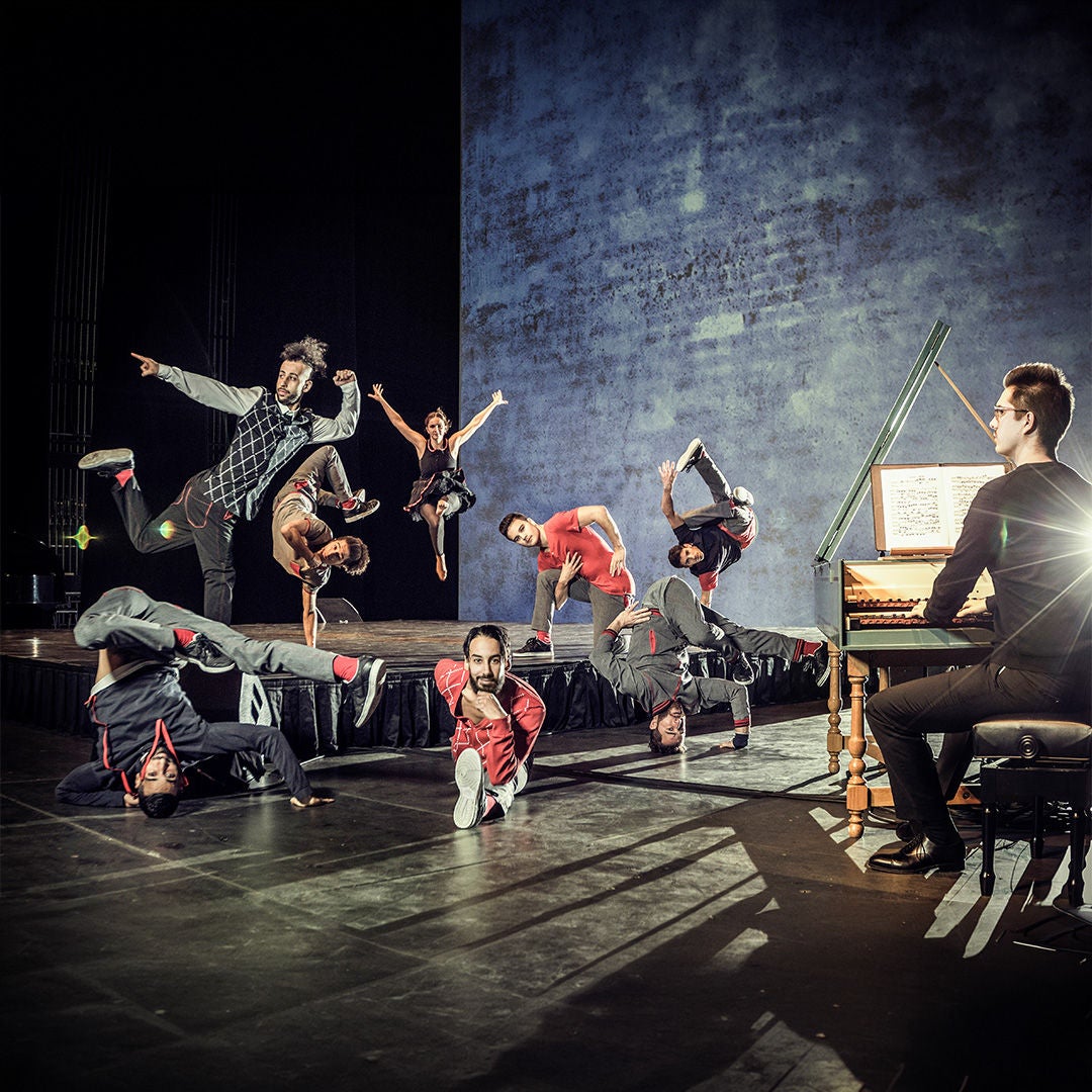 Breakdancer in verschiedenen Posen auf einer Bühne, begleitet von einem Cembalospieler; dynamische Bühnenperformance.