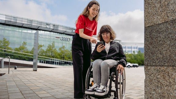 Audi employee shows a woman in a wheelchair something on her smartphone