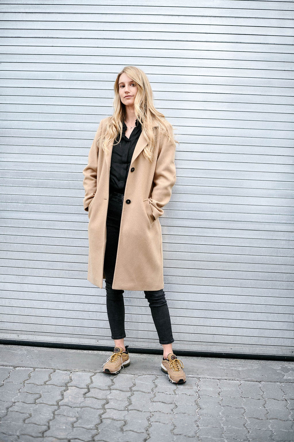 Anna Gasser dans un manteau beige, appuyée contre une porte de garage.