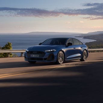 Audi S5 Berline bleue roulant sur une route côtière au coucher du soleil