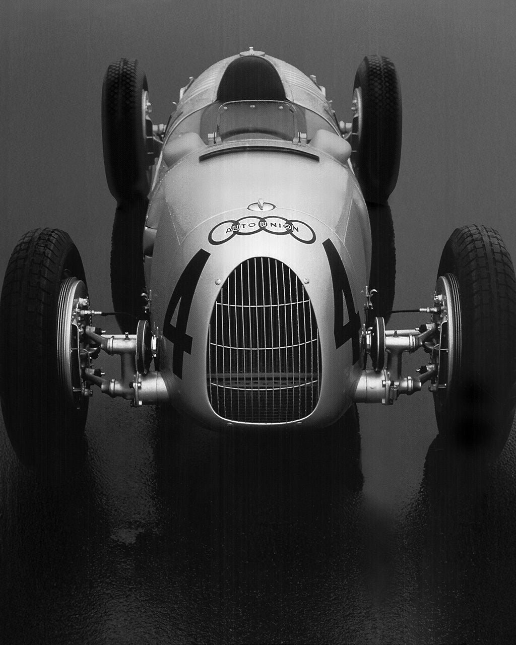Frontansicht eines historischen Audi Rennwagens mit freistehenden Rädern vor grauem Hintergrund.