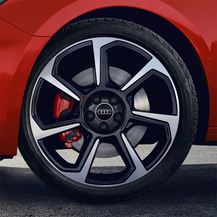A close up of one of the wheels on a red Audi vehicle, red disc brake also visible
