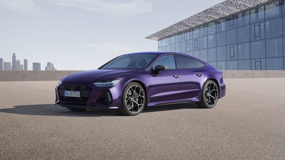 A purple sedan parked in front of a modern building with a city skyline in the background.