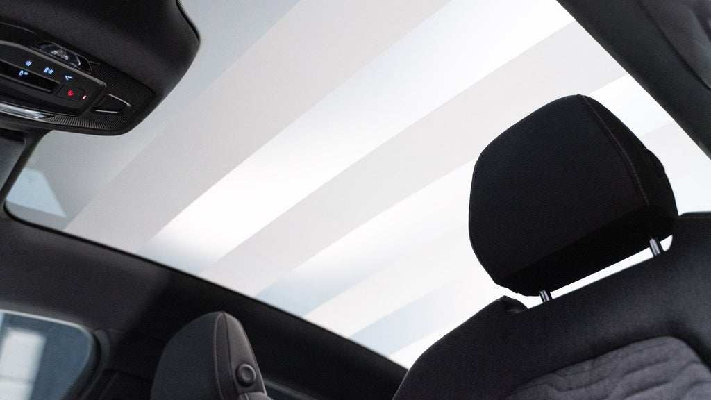 Het glazen panoramadak van de Audi A6 Sportback e-tron vanuit de bestuurdersstoel bekeken. Van die stoel is de hoofdsteun te zien. De bedieningsunit is links zichtbaar.