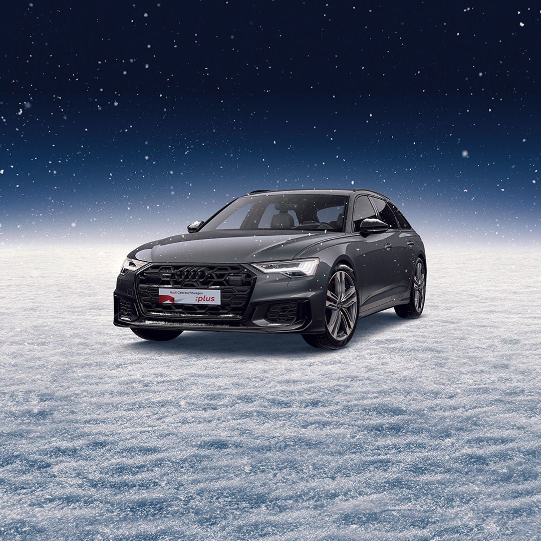 Ein grauer Audi A6 steht auf einem schneebedeckten Untergrund, während es schneit.