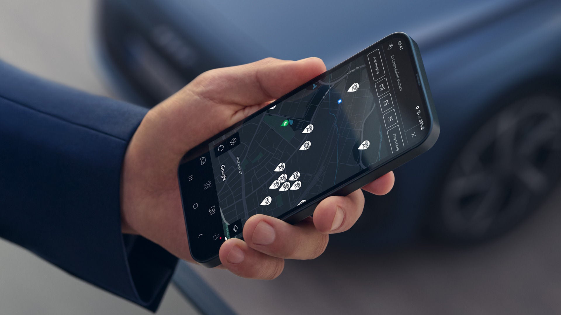 Smartphone in einer Hand mit geöffneter Navigations-App, die nahegelegene Ladestationen auf einer Karte anzeigt.