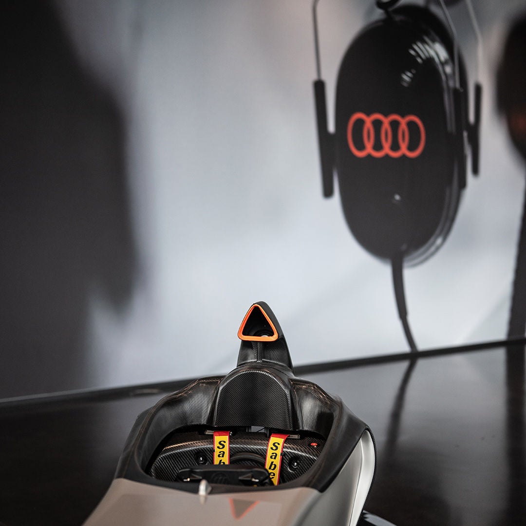Nahaufnahme eines Audi racing Simulators mit gelben Gurten; darüber hängt ein schwarzer Kopfhörer mit Audi-Ringen.