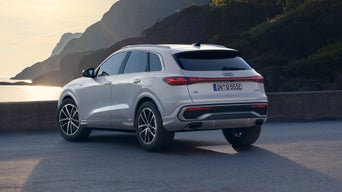 Der Q5 SUV schräg von hinten auf einem Parkplatz direkt am Meer, im Hintergrund ragen bewaldete Berge hervor.