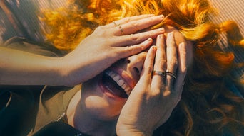 Eine Frau lacht und verdeckt dabei mit ihren Händen ihre Augen.