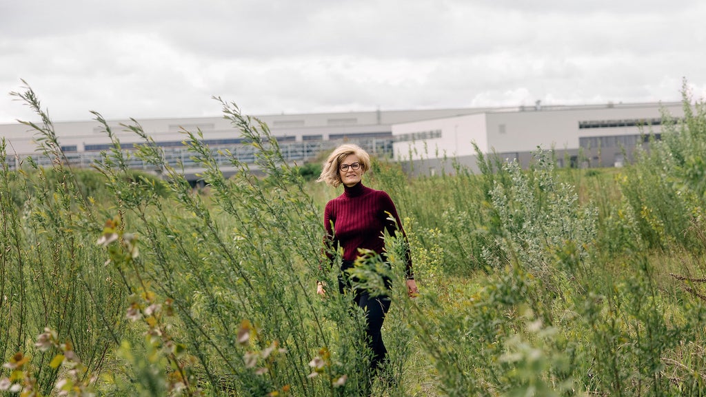 Dr. Antje Arnold stands in a flowering area and smiles, with a building in the background