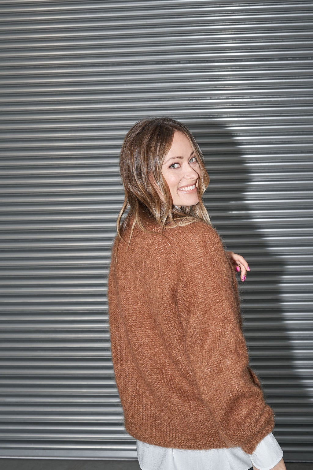 Le dos à moitié tourné, Olivia Wilde rit face à la caméra.