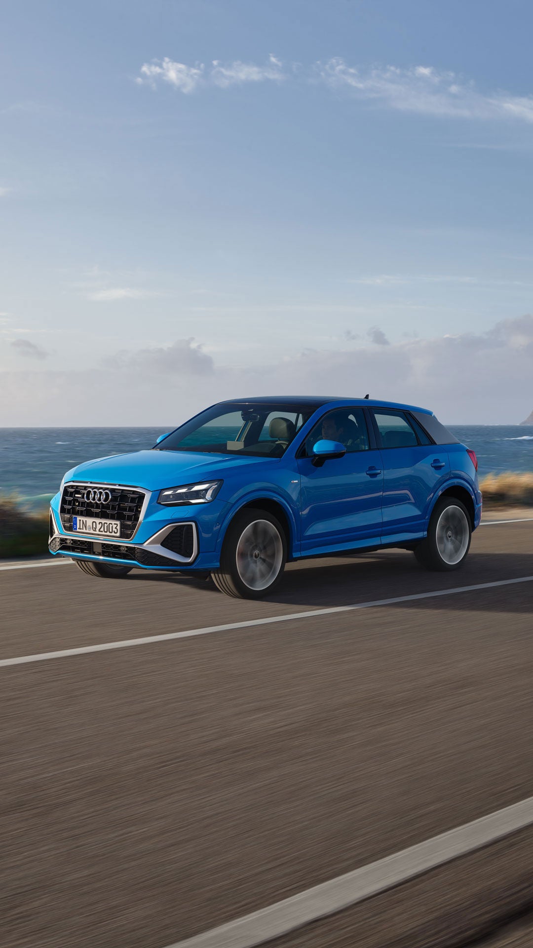 Ein blauer Audi fährt auf einer Straße direkt am Wasser vor einer Küstenlandschaft.