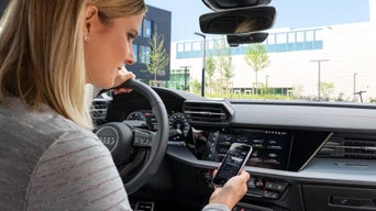 Eine Frau sitzt in einem Audi und schaut auf ihr Handy