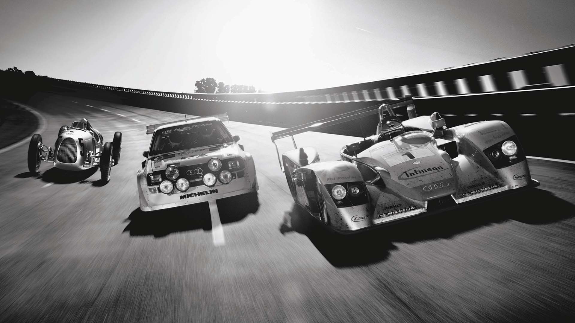 A picture showing three historic Audi race cars side by side on a banked racetrack.