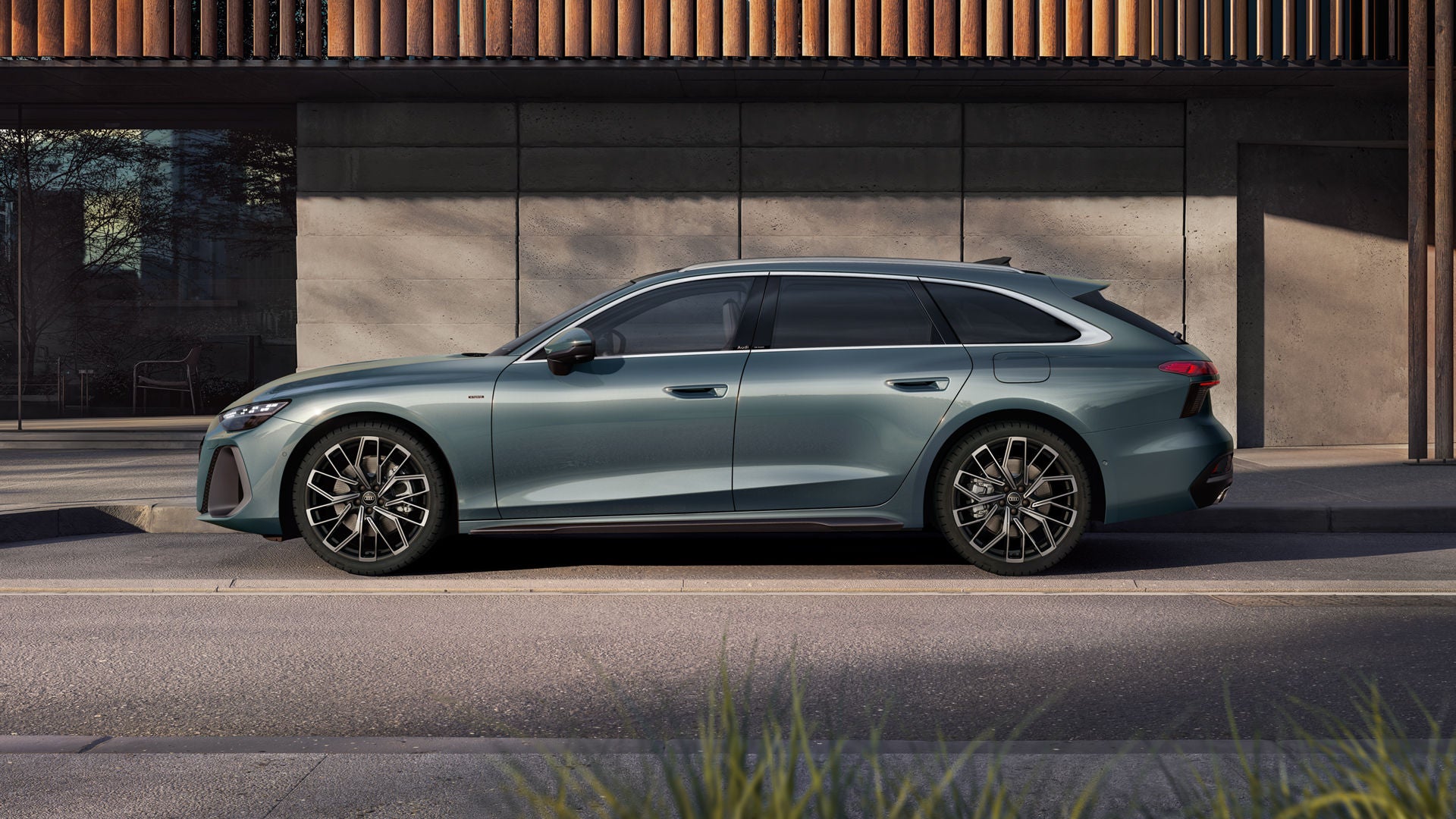 The A6 Avant e-hybrid in morning dew, pearl effect stands in profile in front of a building facade.