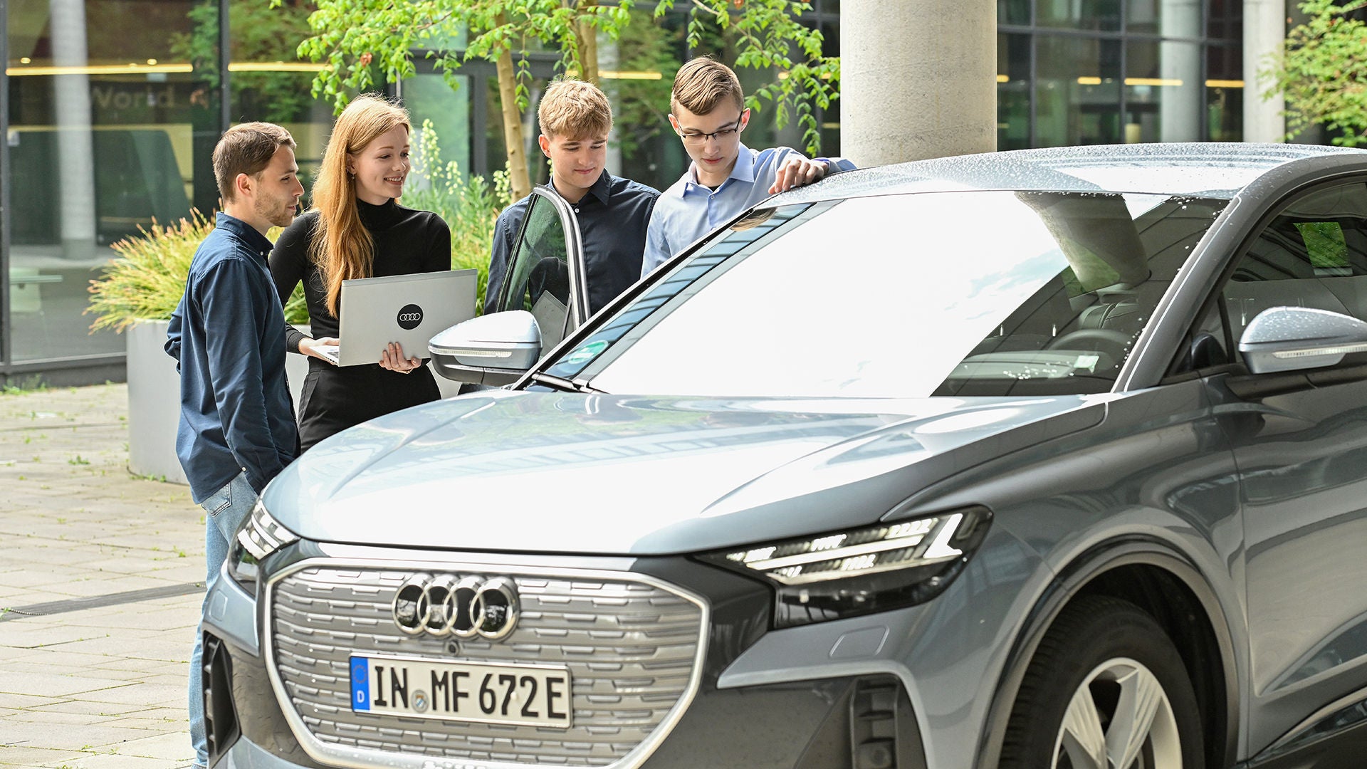 Vier Mitarbeitende von Audi sind im Gespräch und stehen hinter einem Audi 