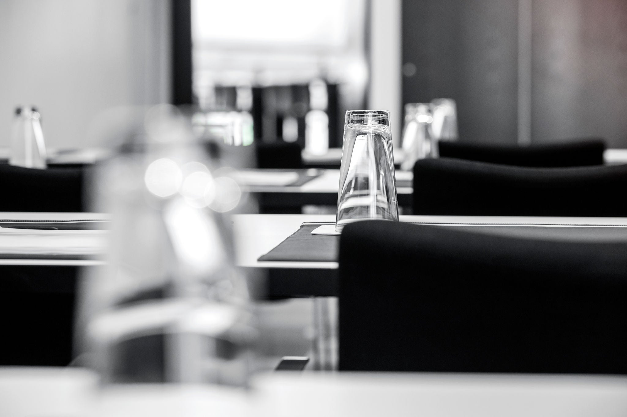 Schwarz-Weiß-Foto eines gedeckten Restauranttisches mit umgedrehtem Wasserglas und unscharfen Tischen im Hintergrund.