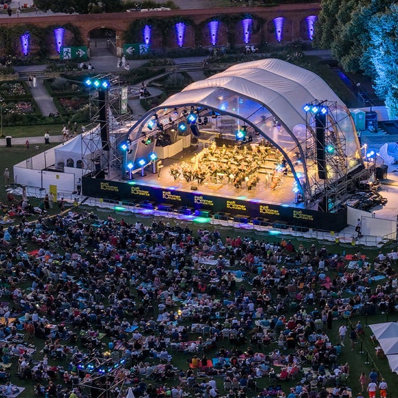 Open-Air-Konzert bei Nacht mit großer Bühne, bunten Lichtern und vielen Zuschauern auf einer Wiese.