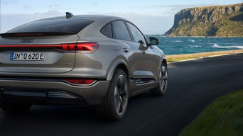 Grauer, elektrisch angetriebener Audi SUV-Coupé in Heckansicht auf Küstenstraße; rechts Meer, vorn Felsklippe, blauer Himmel.