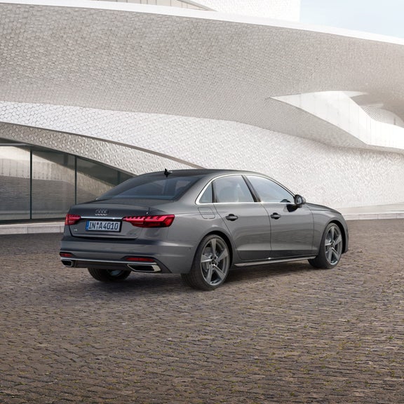 A grey Audi A4 sedan parked in front of a modern building with a unique geometric facade.