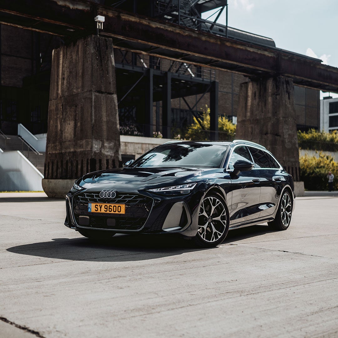 Audi A6 e-tron steht auf einem Schotterhof vor einem beigen Haus mit weißen Fensterläden.