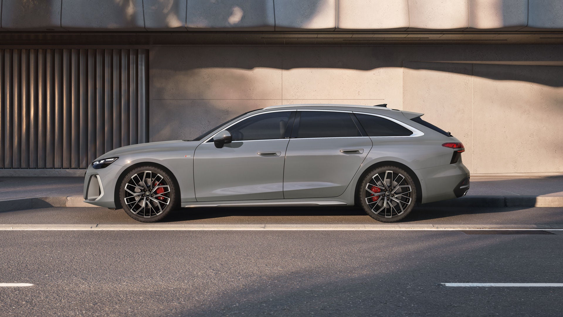The A6 Avant is parked in a parking bay in front of a building facade, viewed from the side and painted gray.