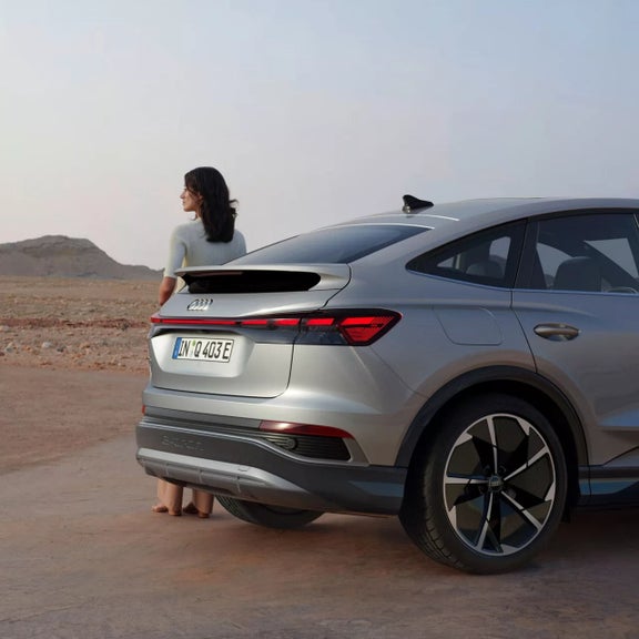 An Audi Q4 Sportback e-tron parked on rugged terrain, a woman is standing beside the rear of the car 