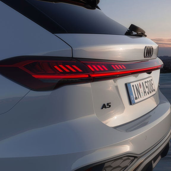 Close-up of a white Audi A5 e-hybrid rear with sleek, glowing red taillights and a European license plate.