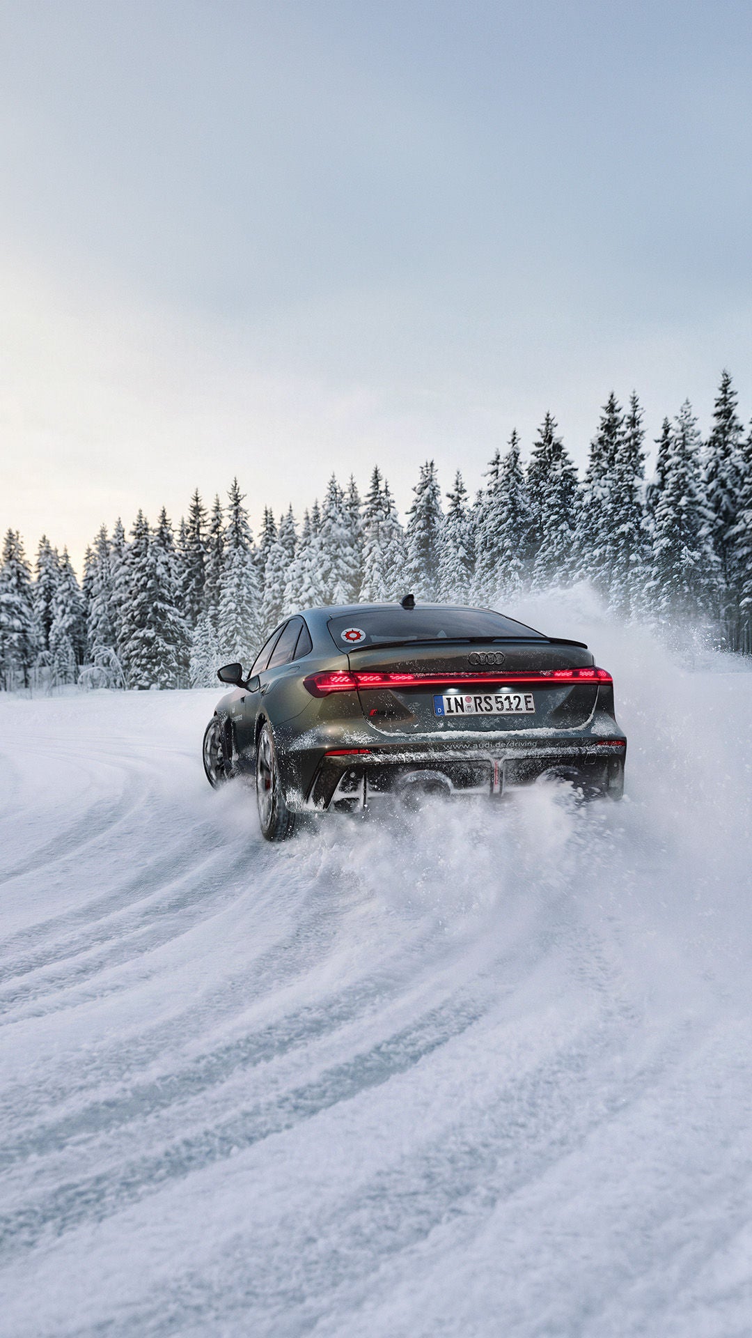 A dark green Audi RS 5 sedan drives along a snow-covered road; snow dust, a pine forest, and a blue sky.