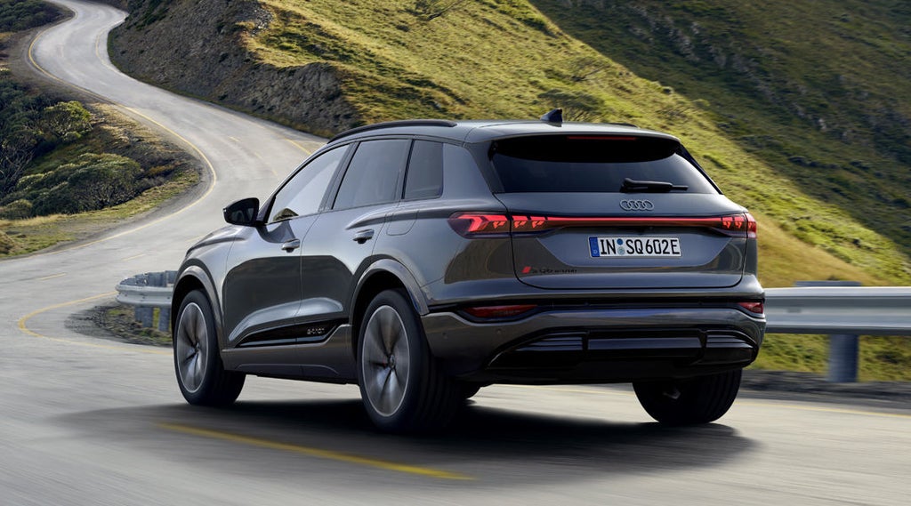 Achteraanzicht van de SQ6 SUV e-tron rijdend over bochtige wegen in een bergachtig landschap.