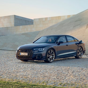An electric sedan car charging at a station with a minimalist building backdrop at dusk.