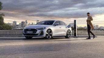 Die A5 Limousine e-hybrid ist an eine Ladestation angeschlossen. Im Hintergrund ist die Skyline einer Stadt bei Dämmerung zu sehen.