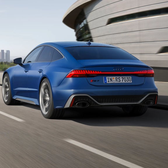 A blue car driving on a road, captured from the rear three-quarter angle.