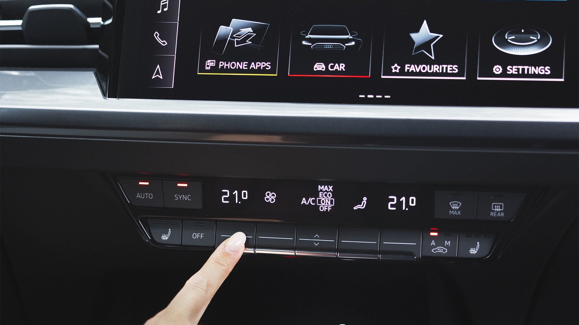 Finger berührt Klimabedienfeld eines Audi, oberhalb ist ein Display mit Infotainment-Icons wie "Car" und "Phone Apps" sichtbar.