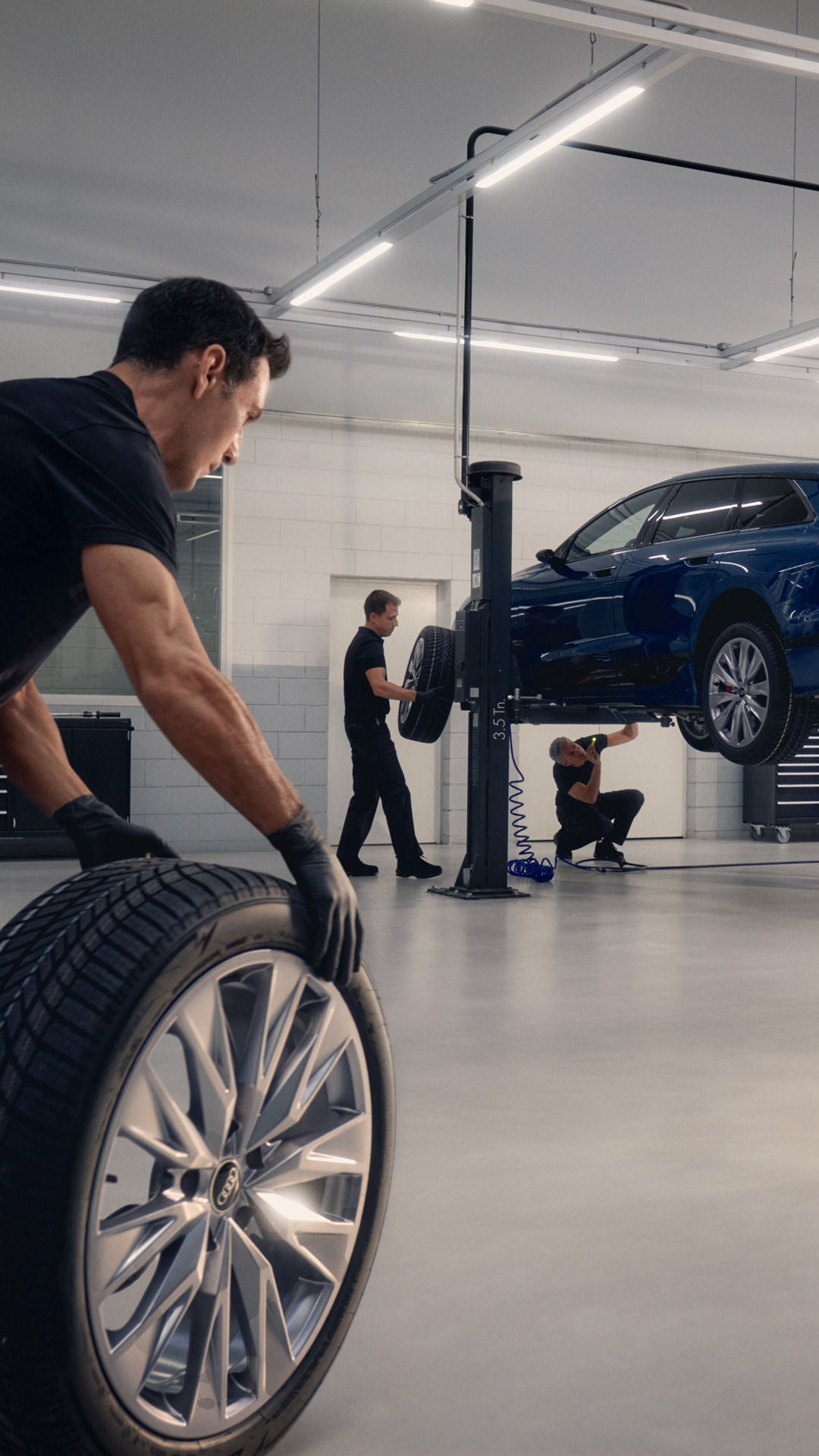 Ein Audi Mitarbeiter rollt einen Reifen durch eine Werkstatt. Im Hintergrund sind Audi Modelle an Hebebühnen.