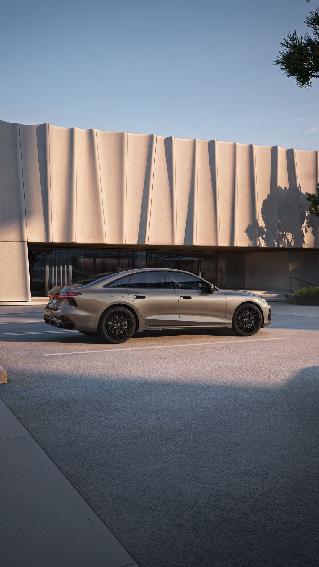Die A6 Limousine in Dakotagrau Metallic steht im Seitenprofil auf einem Parkplatz vor einem großen, modernen Gebäude.