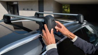 Mani su una delle due barre porta carico montata sul tettuccio di un veicolo Audi