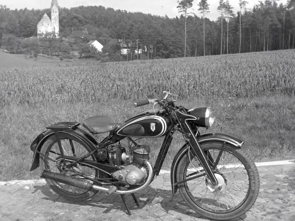 Schwarz-weiße Seitenaufnahme einer DKW RT 125 W vor einem Feld am Hang