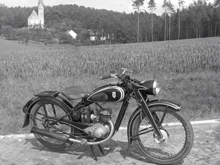 Black and white side view of a DKW RT 125 W in front of a field on a slope