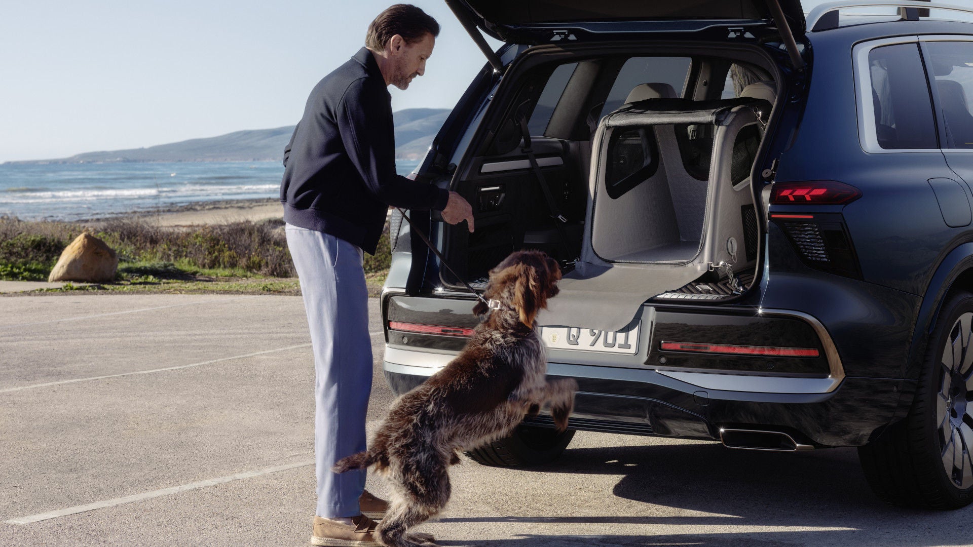 Man laat zijn hond in de bench springen die achter in de Audi Q9 staat.