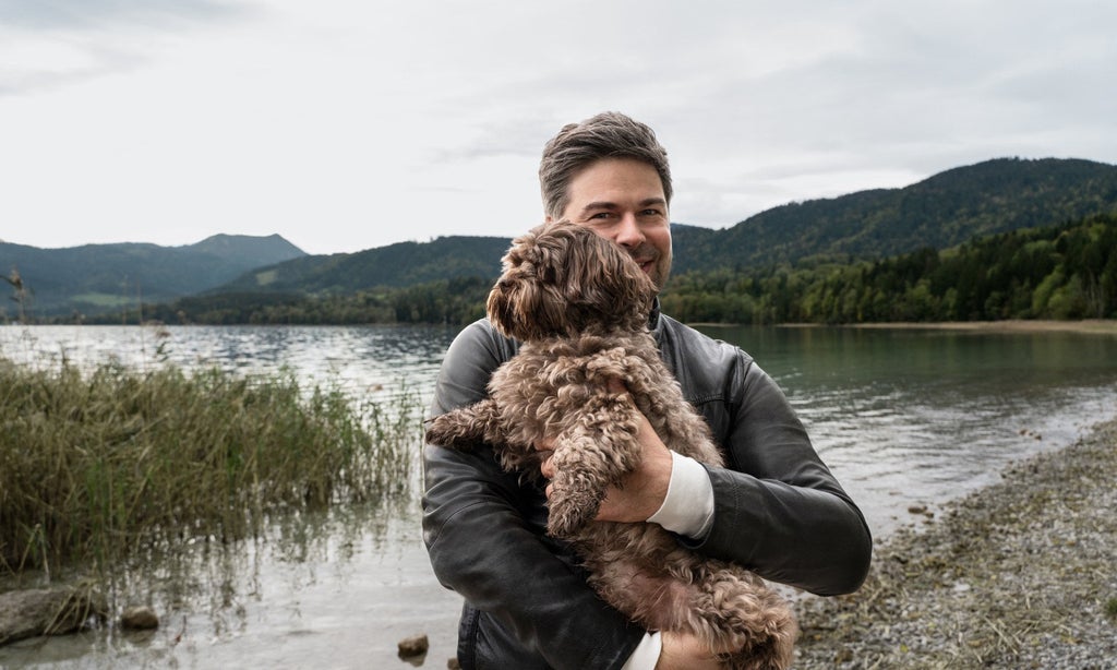 Nils Wollny standing by the lake with his dog in his arms.
