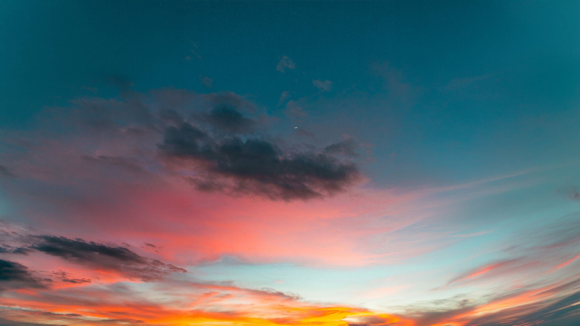 Abendhimmel mit farbigem Sonnenuntergang in Orange, Rosa und Türkis sowie dunklen Wolken und einer schmalen Mondsichel.