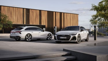 Audi A6 Avant e-hybrid quattro and Audi A6 Sedan e-hybrid quattro at charging stations in front of a modern building with a facade made of wood panels.
