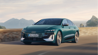 A green Audi car driving on a coastal road with mountains in the background.