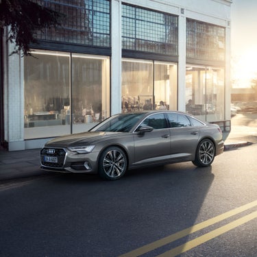 A sedan car parked on a city street at sunset, in front of a glass-walled building