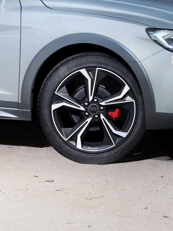 Nahaufnahme einer schwarzen und silbernen Audi-Felge mit rotem Bremssattel auf Asphalt.