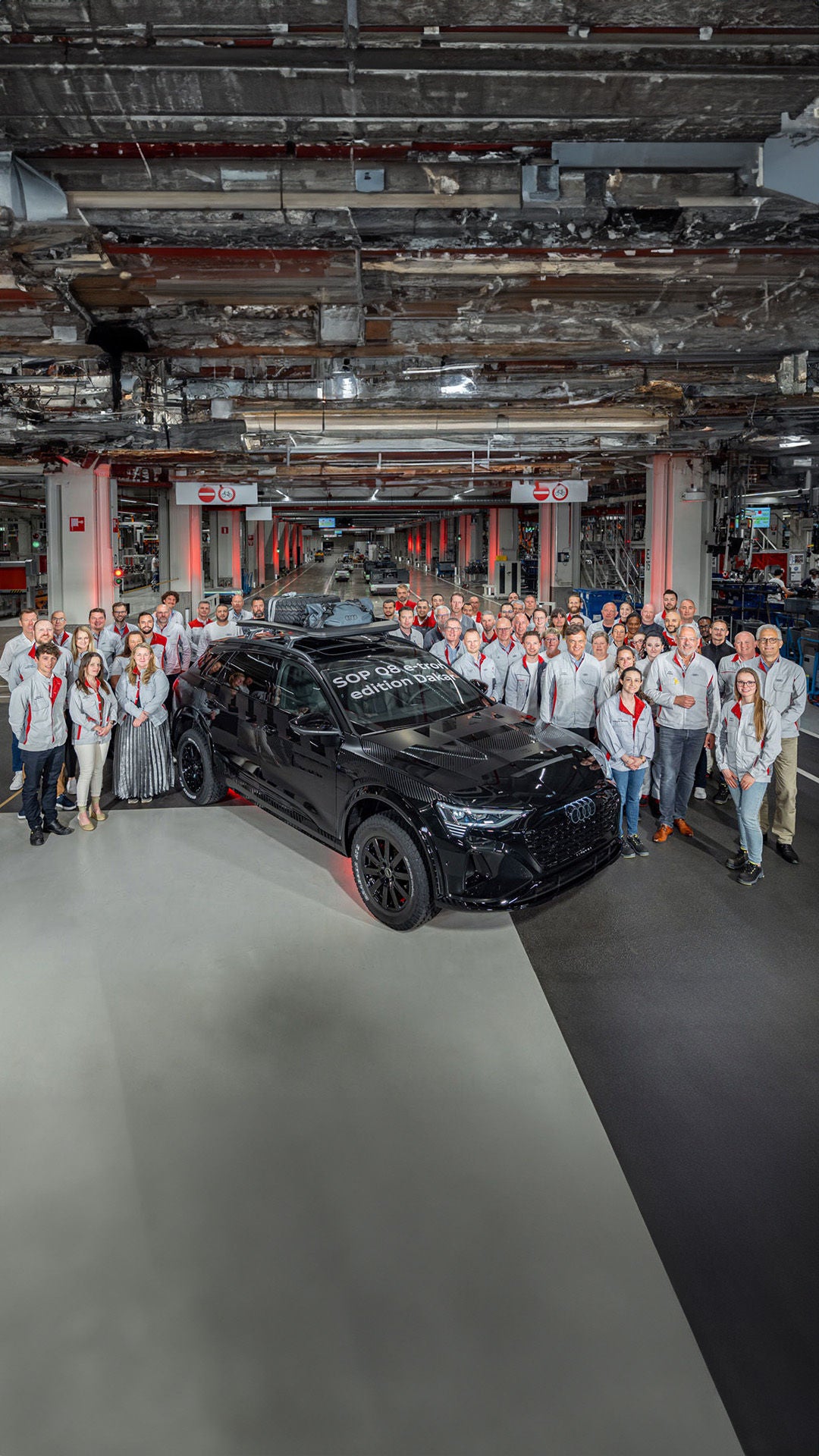 Des employés se tiennent à côté d'une Audi Q8 e-tron édition Dakar noire à l'usine.