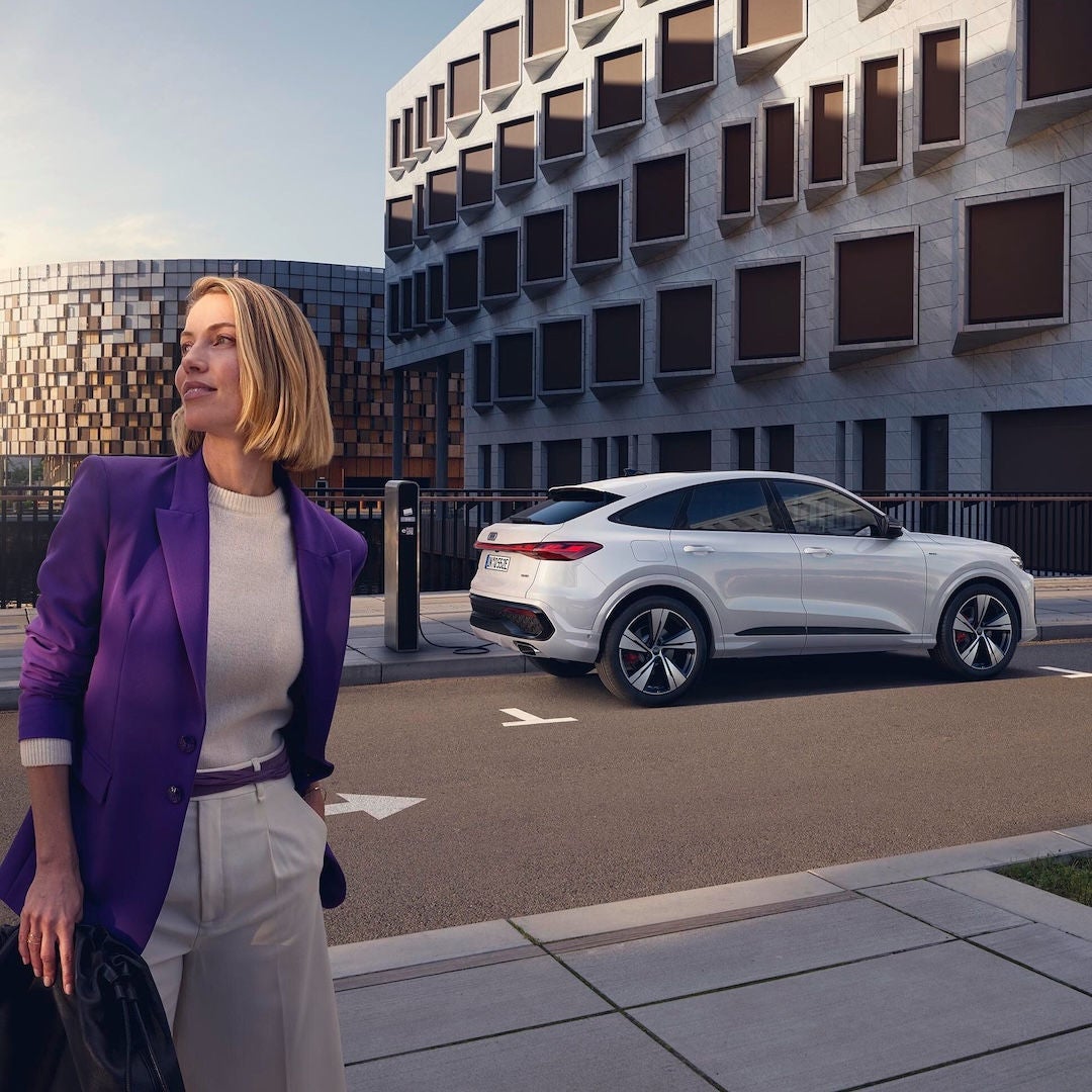 Una donna e sullo sfondo Audi Q5 Sportback e-hybrid parcheggiata e collegata a una colonnina di ricarica