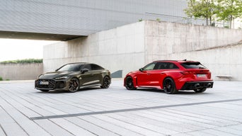 The Audi RS 5 Sedan and Audi RS 5 Avant—one in Bedford Green Metallic, the other in Progressive Red Metallic—are parked on a stone surface.
